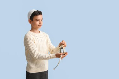 Little Muslim boy with fanous lantern and praying beads on light blue background