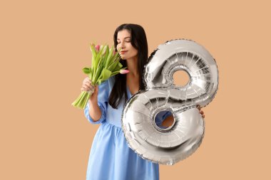 Şekil 8 şeklinde gümüş renkli balonu ve kahverengi arka planda güzel laleleri olan güzel bir kadın. Uluslararası Kadınlar Günü