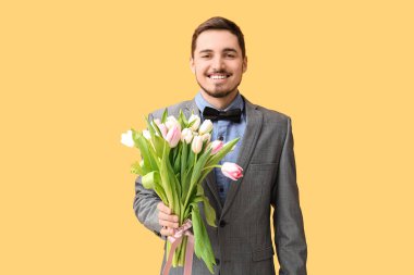 Sarı arka planda güzel lalelerle dolu buketi olan mutlu genç bir adam. Uluslararası Kadınlar Günü