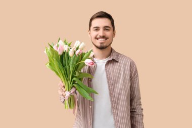 Bej arka planda bir buket lalesi olan mutlu genç bir adam. Uluslararası Kadınlar Günü