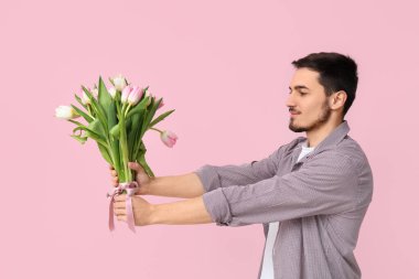 Pembe arka planda bir buket güzel lalesi olan genç bir adam. Uluslararası Kadınlar Günü