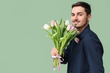 Yeşil arka planda güzel lalelerle dolu buketi olan mutlu genç bir adam. Uluslararası Kadınlar Günü