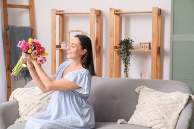 Evdeki kanepede güzel lalelerle dolu buketi olan mutlu genç bir kadın. Uluslararası Kadınlar Günü