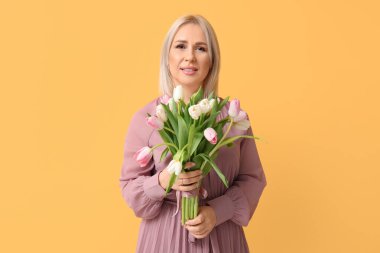 Sarı arka planda bir buket güzel lalesi olan olgun bir kadın. Uluslararası Kadınlar Günü