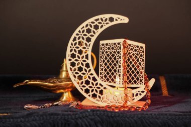 Ramazan için dekoratif hilal, yanan mum, dua boncukları ve Aladdin lambalı mavi hasırlı koyu arkaplan