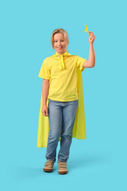 Mavi arka planda altın kurdeleli süper kahraman gibi giyinmiş küçük bir kız. Çocukluk kanseri farkındalığı