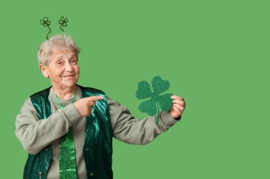 Saç bantlı yaşlı kadın yeşil arka plandaki yoncayı işaret ediyor. Aziz Patrick Günü kutlaması