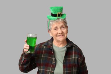 Gri arka planda bir bardak birayla cüce şapkalı yaşlı kadın. Aziz Patrick Günü kutlaması