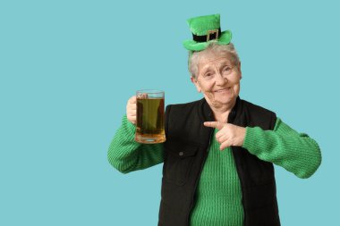 Leprikon şapkalı yaşlı kadın mavi arka planda bir bardak biraya bakıyor. Aziz Patrick Günü kutlaması