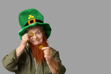 Kırmızı sakallı cüce şapkalı yaşlı kadın gri arka planda bozuk para tutuyor. Aziz Patrick Günü kutlaması