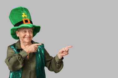 Leprikon şapkalı yaşlı kadın gri arka plandaki bir şeyi işaret ediyor. Aziz Patrick Günü kutlaması
