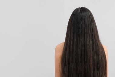 Gri arka planda sağlıklı uzun saçları olan güzel bir genç kadın.