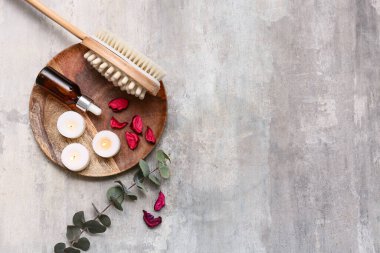 Ahşap tepsi, vücut masajı fırçası, bir şişe serum, gül yaprakları ve arkaplandaki mumlarla güzel bir kompozisyon.