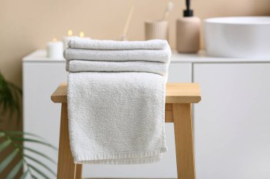 Modern banyonun iç tarafındaki ahşap masanın üzerinde temiz, yumuşak havlular yığını.
