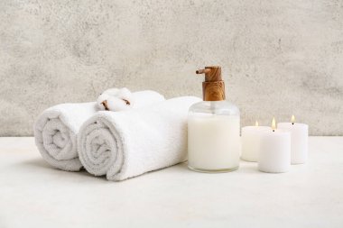 Temiz yumuşak havlular, bir şişe kozmetik ürünü ve banyoda grunge duvarının yanında mumlar.