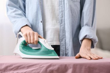 Kadın evde temiz çamaşır ütülüyor.