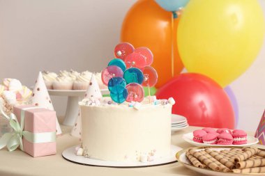 Beyaz duvara karşı pasta, şeker ve doğum günü partisi için dekorasyon masası.