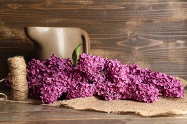 Tahta arka planda iple ve sürahiyle çiçek açan leylak çiçekleri