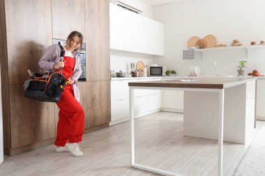 Mutfakta elektrikli fırının yanında alet çantası taşıyan kadın teknisyen.