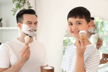 Mutlu baba ve küçük oğlu banyoda yüzlerine tıraş köpüğü sürüyorlar.