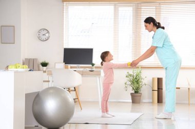 Kadın osteopat ve elastik bantlı küçük bir hasta klinikte egzersiz yapıyor.