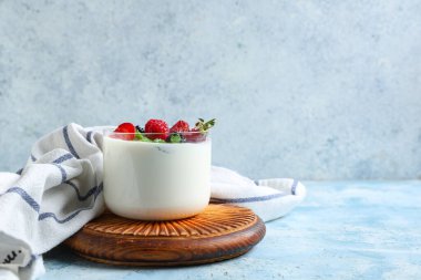 Farklı taze böğürtlenli ve açık mavi arkaplanda naneli bir bardak lezzetli yoğurt.