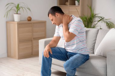 Evdeki kanepede boynundaki ağrıdan muzdarip genç adam.
