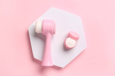 Alçı sehpası, yüz masajı fırçası ve pembe arka planda bir kavanoz kozmetik ürünü.