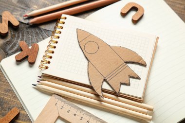 Tahta arka planda farklı okul kırtasiyesine sahip karton roket, yakın plan.