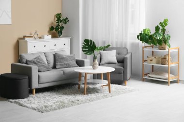 Masada ve şık koltukta tropikal canavar yaprakları olan modern bir oturma odası.