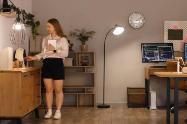 Tablet bilgisayarlı genç iş kadını geceleri ofiste kahve yapıyor.