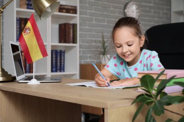 Bilgisayarı olan küçük bir kız, İspanya bayrağı ve evde İspanyolca dersine katılan bir defter.