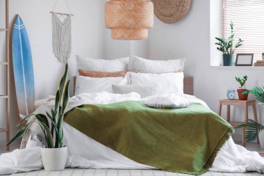 Büyük rahat bir yatak, raf ünitesi, sörf tahtası ve yatak odasının iç kısımlarında bitkiler.