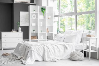 Büyük rahat bir yatak, çekmeceler, raf ünitesi ve yatak odasının içindeki komodin.