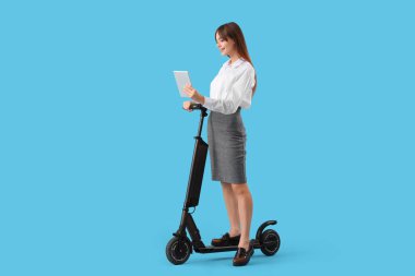 Modern elektrikli scooter 'ı ve mavi arka planda tablet bilgisayarı olan güzel genç bir iş kadını.