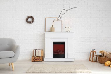 Modern şöminesi, koltuğu ve beyaz tuğla duvarın yanında sonbahar süslemeleri olan şık bir oda.