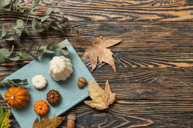 Balkabağı, kitap, sonbahar yaprakları şeklinde mumlar ve okaliptüs dallı ahşap zemin.