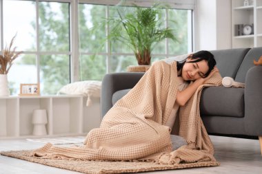 Güzel, genç, mutlu bir kadın. Sıcak ekose ve kulaklıklı. Evde yerde oturuyor.