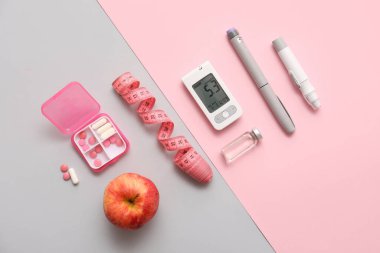 Neşter kalemli modern glukometre, insülin ampulü, mezura, elma ve renkli arkaplan hapları.
