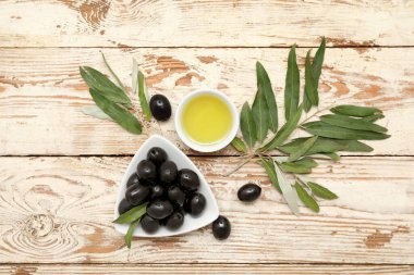 Lezzetli siyah zeytinli tabak ve hafif ahşap arka planda bir kase yağ.