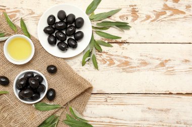 Lezzetli siyah zeytinli tabak ve hafif ahşap arka planda bir kase yağ.