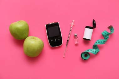 Şırıngalı modern glukometre, insülin ampulü, elmalar ve pembe arka planda mezura.