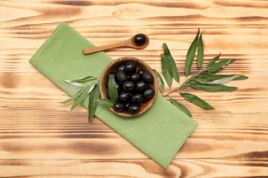 Lezzetli siyah zeytinli kase, kaşık ve yapraklı ahşap arka plan