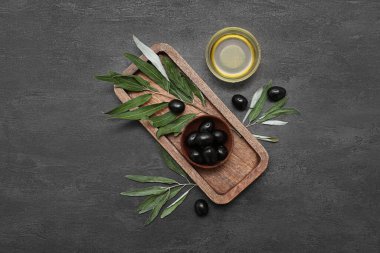 Lezzetli siyah zeytin kâseleri ve siyah grunge arkaplanda yağlı ahşap tepsi.