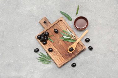 Lezzetli siyah zeytinli ahşap tahta ve gri arka planda bir kase yağ.