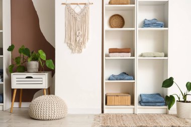 Odadaki ışık duvarının yanında giysi, dekor ve çiçek rafları var.