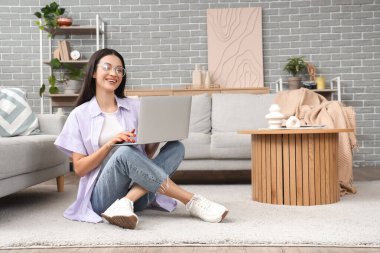 Evdeki halıda dizüstü bilgisayar kullanan güzel bir kadın.