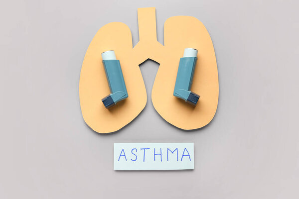 Ингаляторы, бумажные легкие и бумажный лист с текстом ASTHMA на сером фоне