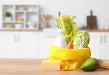 Mutfaktaki ahşap masada farklı taze ürünler bulunan sarı alışveriş çantası.