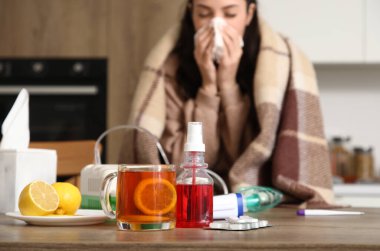 Mutfakta hapşıran hasta kadına karşı masada ilaçlı limon çayı, yakın plan.